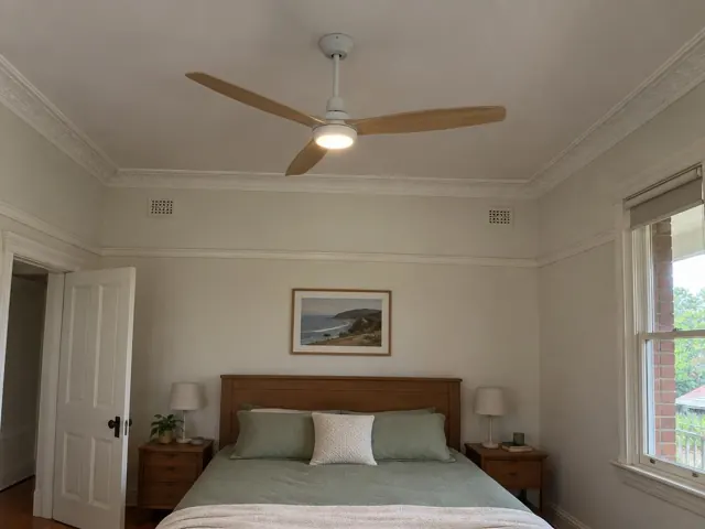 Ceiling fan above a bedroom bed in a cream room with ornate trim and a window in Wyee