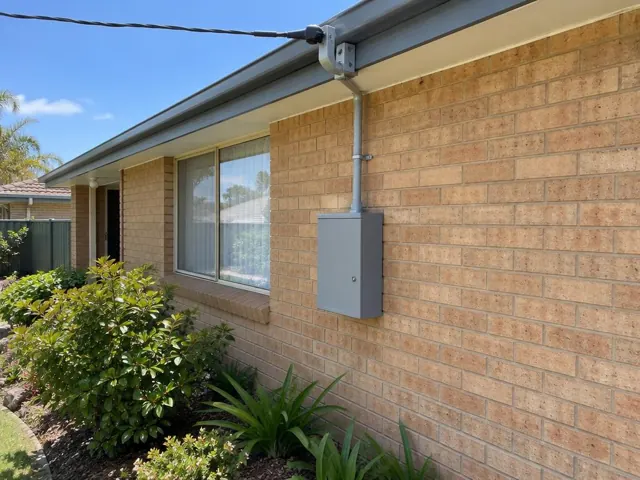 Overhead service cable and point-of-attachment bracket on a brick house exterior in Gwandalan